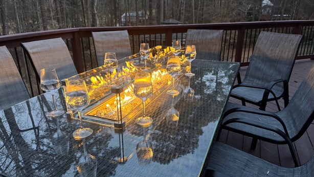 A glass-top dining table with chairs, surrounded by a wooden deck.