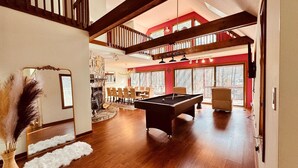 A spacious living area with a pool table, wooden flooring, and a dining area with chairs and a table.