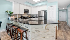 Una cocina moderna con armarios blancos, encimera negra y una isla central con taburetes.