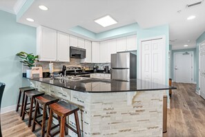 A modern kitchen with white cabinets, a black countertop, and a central island with stools. - San Carlos 703 by Liquid Life (Gulf Shores)