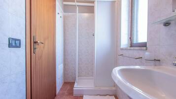 A bathroom with a wooden door, a shower, a sink, and a window.
