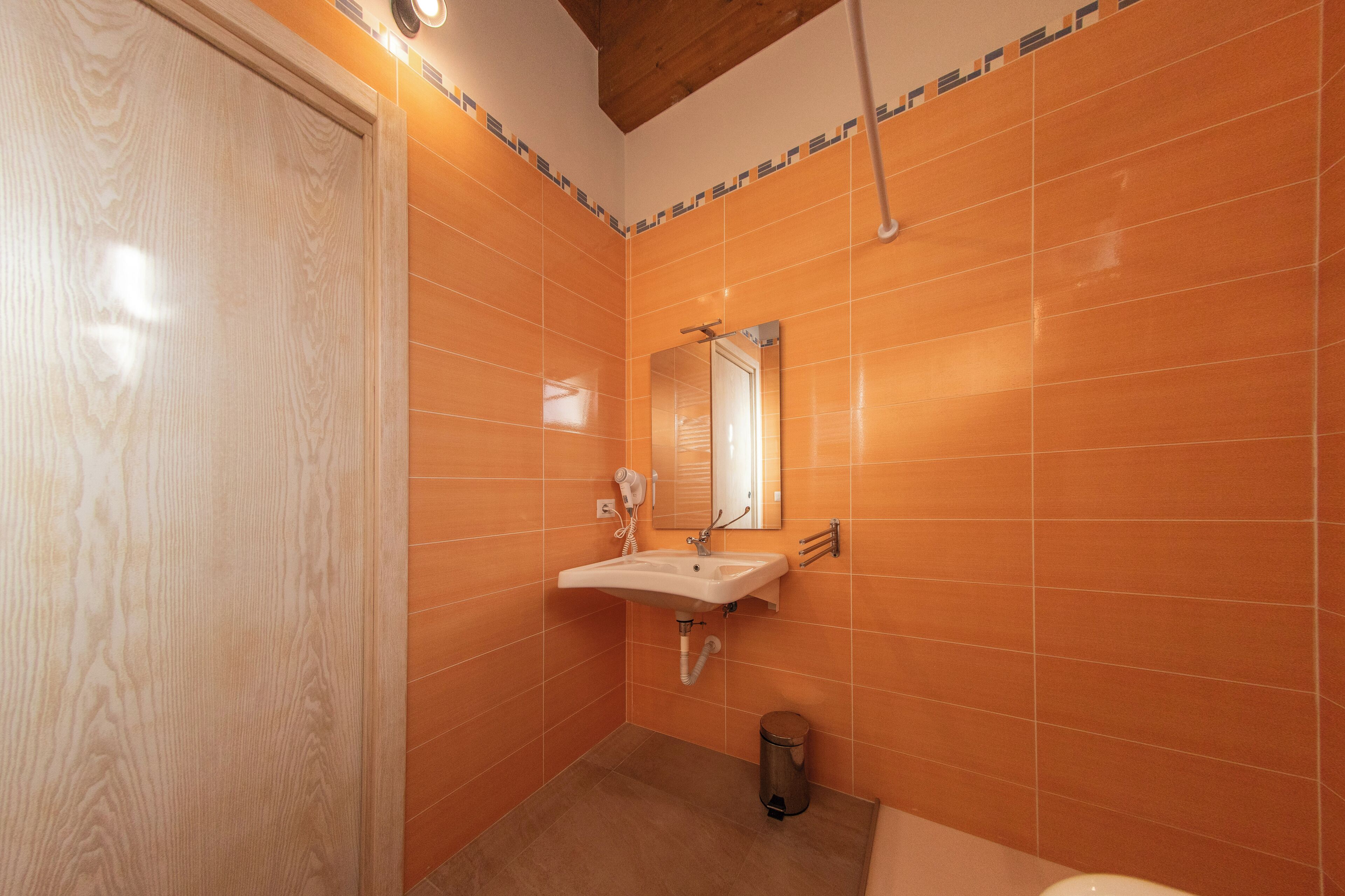 A bathroom with orange tiles, a wooden door, a sink with a mirror, and a shower area.