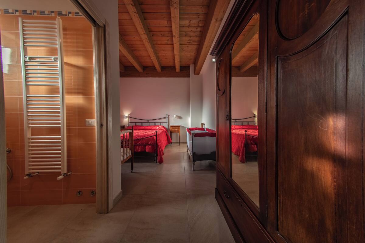Une chambre d’hôtel avec des poutres en bois, une armoire et deux lits avec une literie rouge.