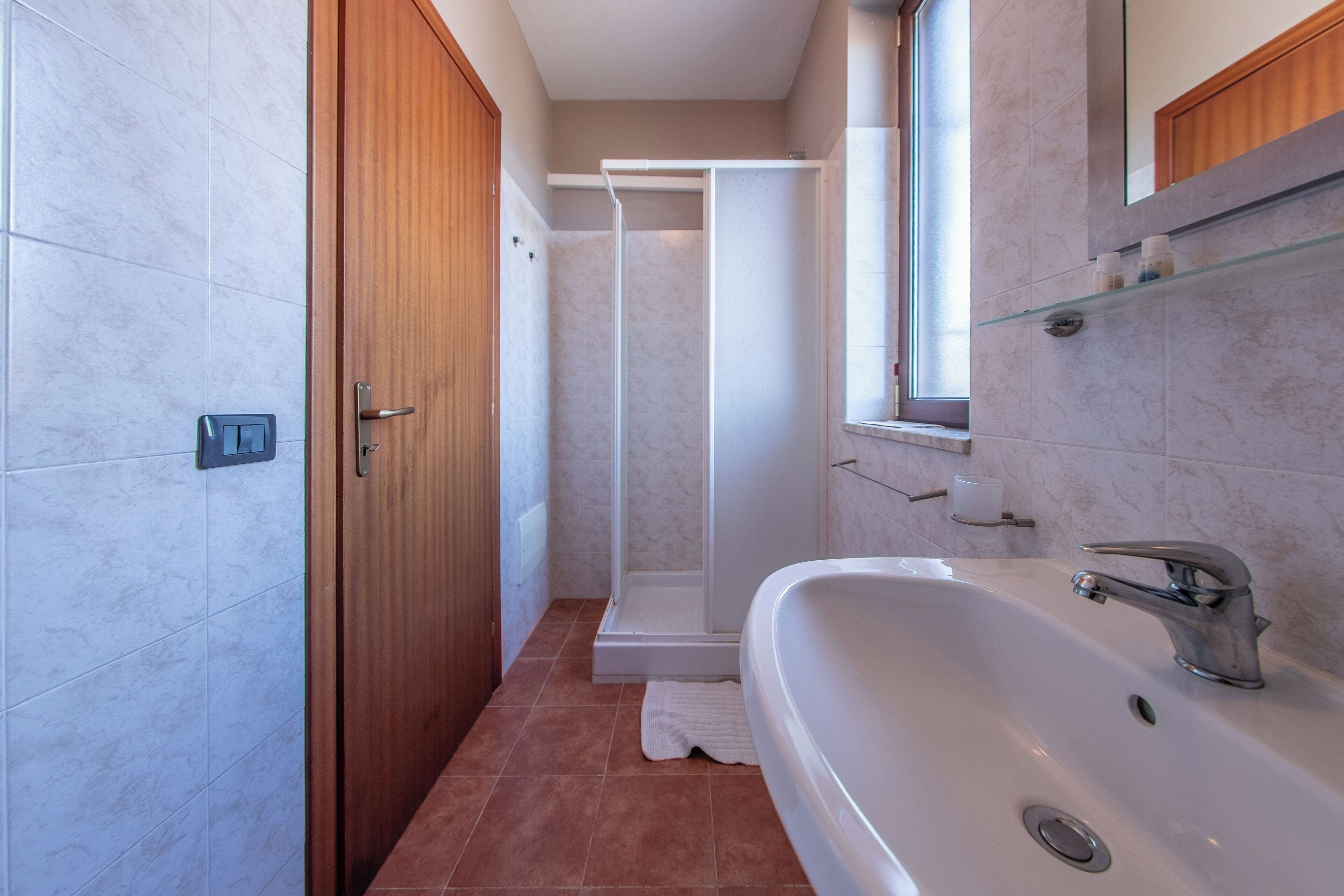 A modern bathroom with a large white sink, a glass shower enclosure, and a wooden door.