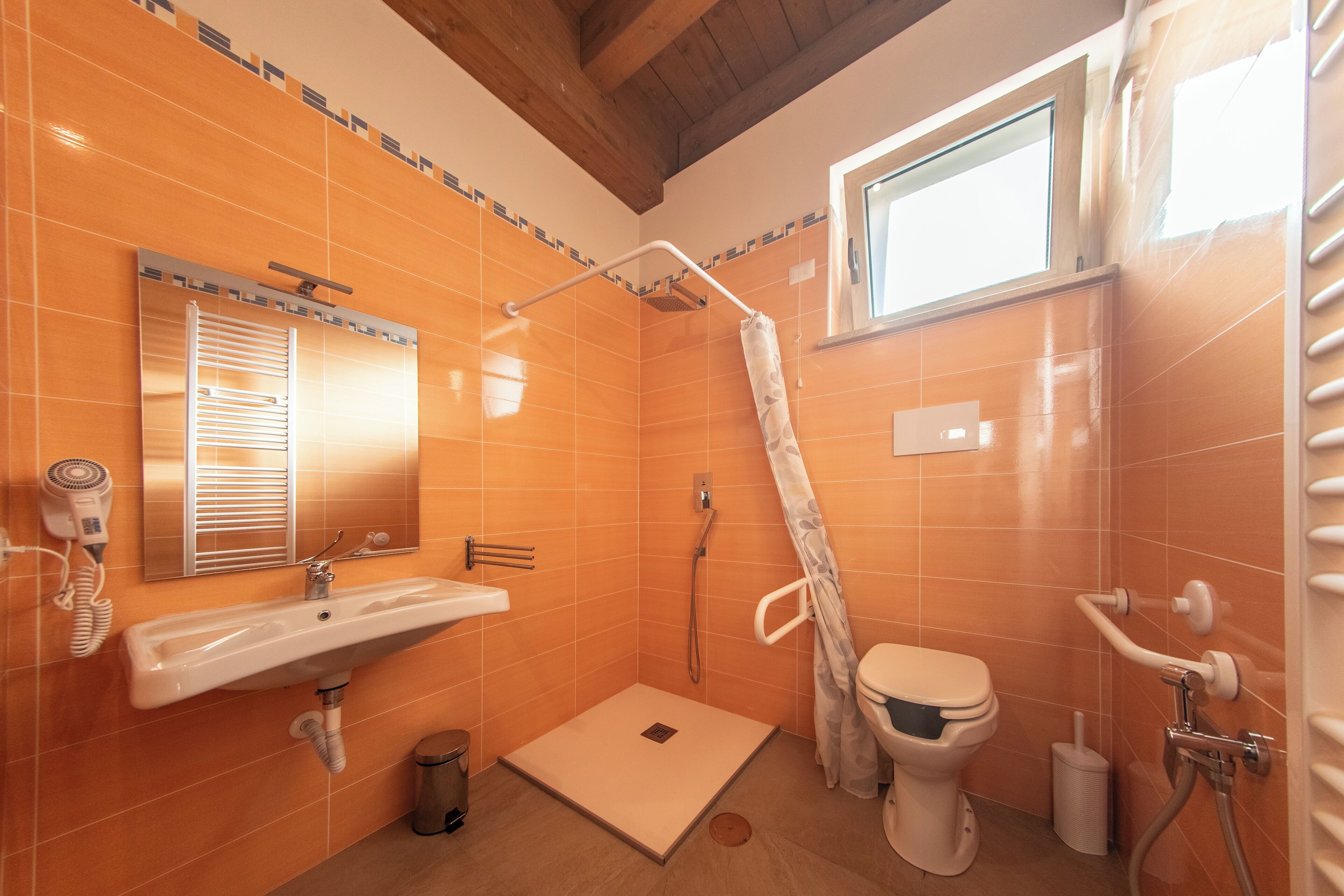 Un baño con azulejos naranja, un lavamanos blanco, ducha, inodoro y ventana.