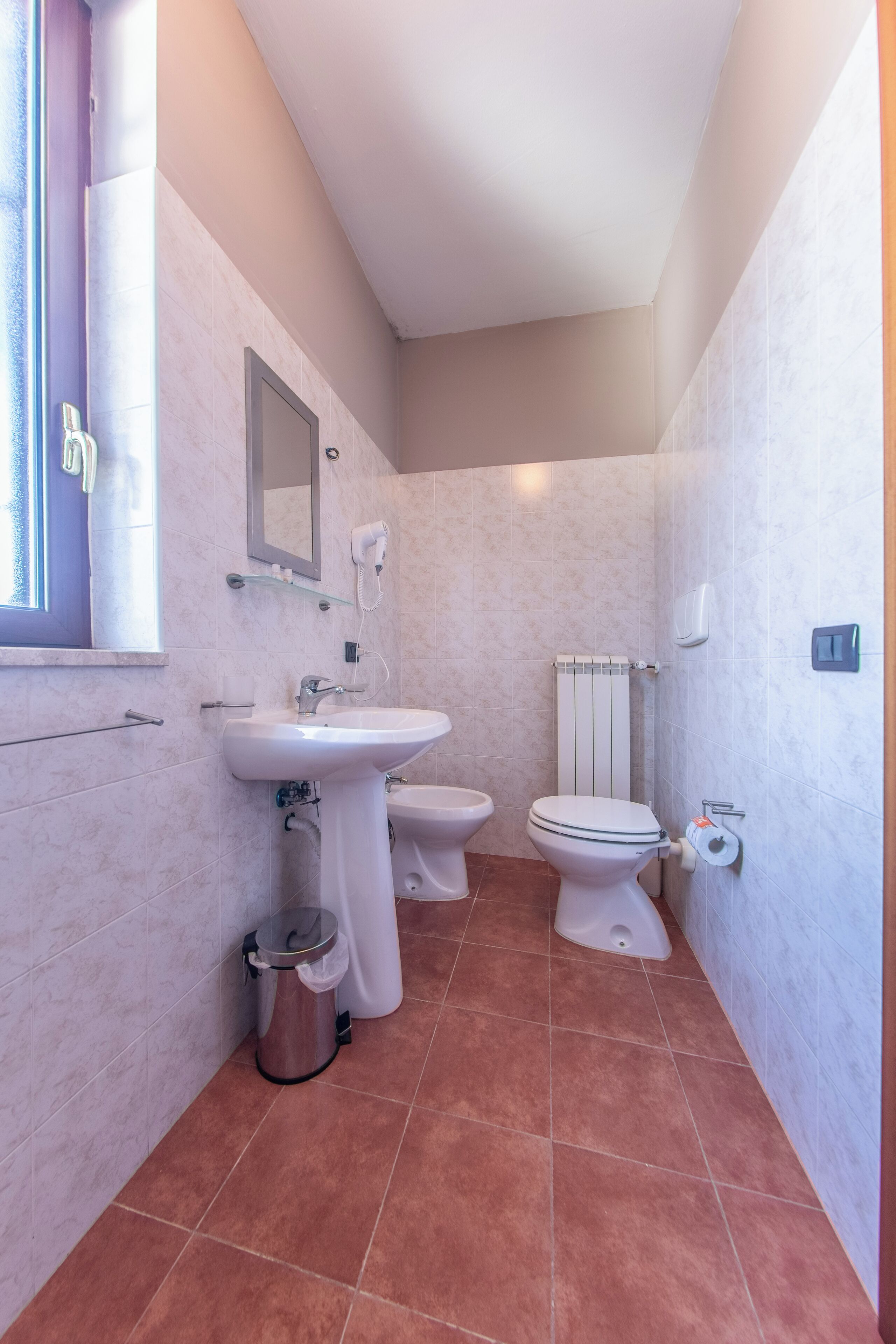 A compact bathroom with a sink, two toilets, and a mirror.