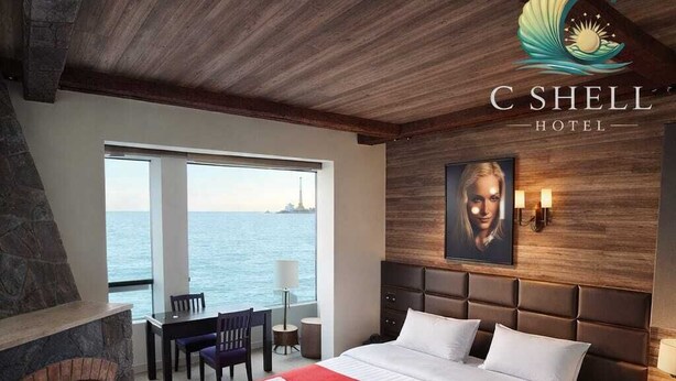 A hotel room with a large bed, a fireplace, a dining area with a view of the sea, and a wooden ceiling.
