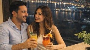 A couple sitting at a bar with drinks, overlooking a cityscape at night.