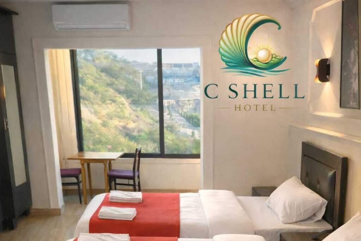 Une chambre d’hôtel avec deux lits, une grande fenêtre donnant sur un beau paysage et un logo sur le mur.