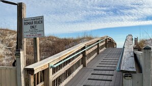 Een houten looppad dat naar een strand leidt, met een bord waarop staat 'Alleen eigenaren en huurders van ROMAR BEACH'.