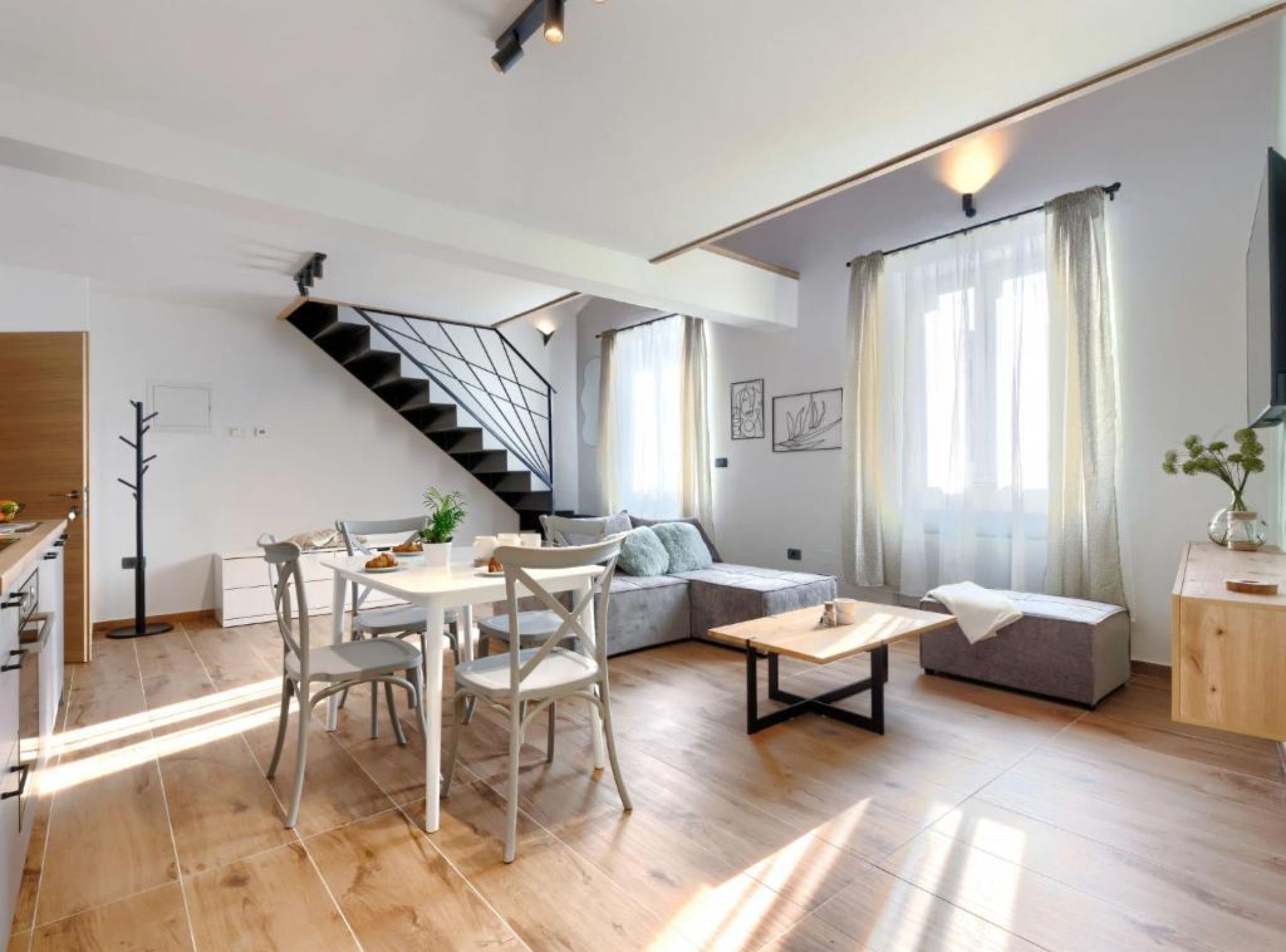A modern living space with a dining area, a staircase, a sofa, and a small table.