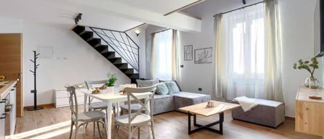 A modern living space with a dining area, a staircase, a sofa, and a small table.