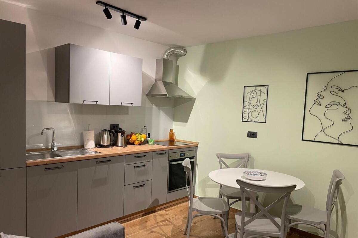 Una cocina moderna con armarios grises, un lavamanos y una estufa. Hay un comedor con una mesa redonda y sillas.