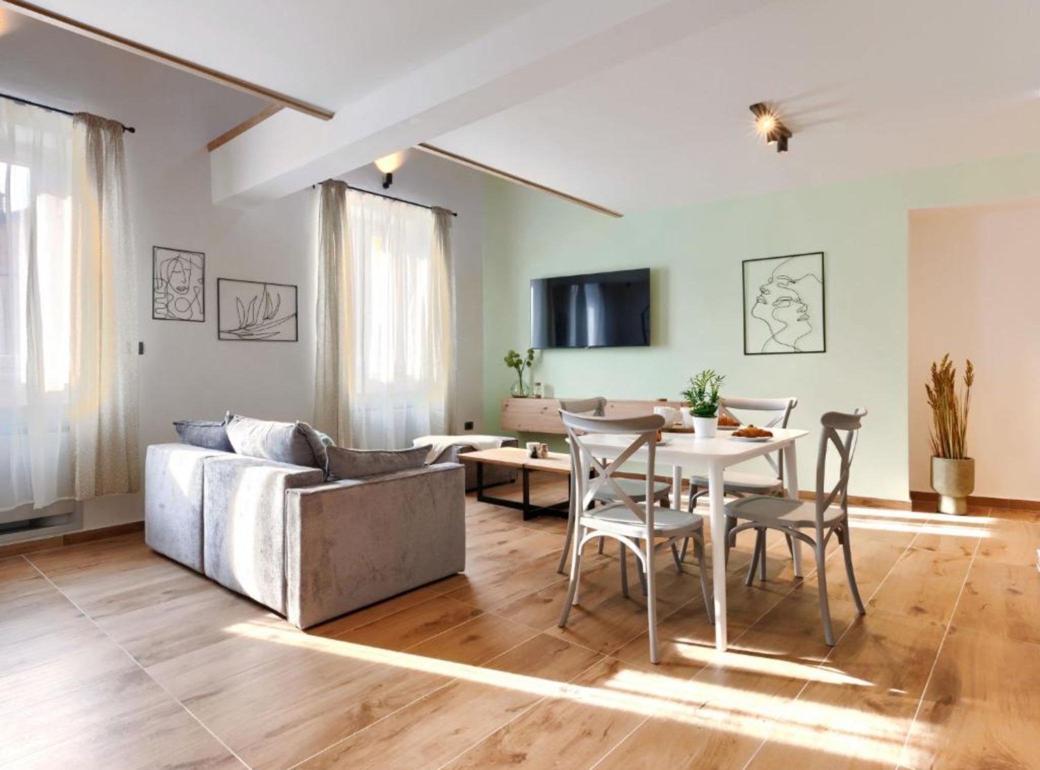 Un salon moderne avec un canapé, une table à manger et des chaises. Un téléviseur à écran plat est fixé au mur, et des œuvres d’art ornent les murs.