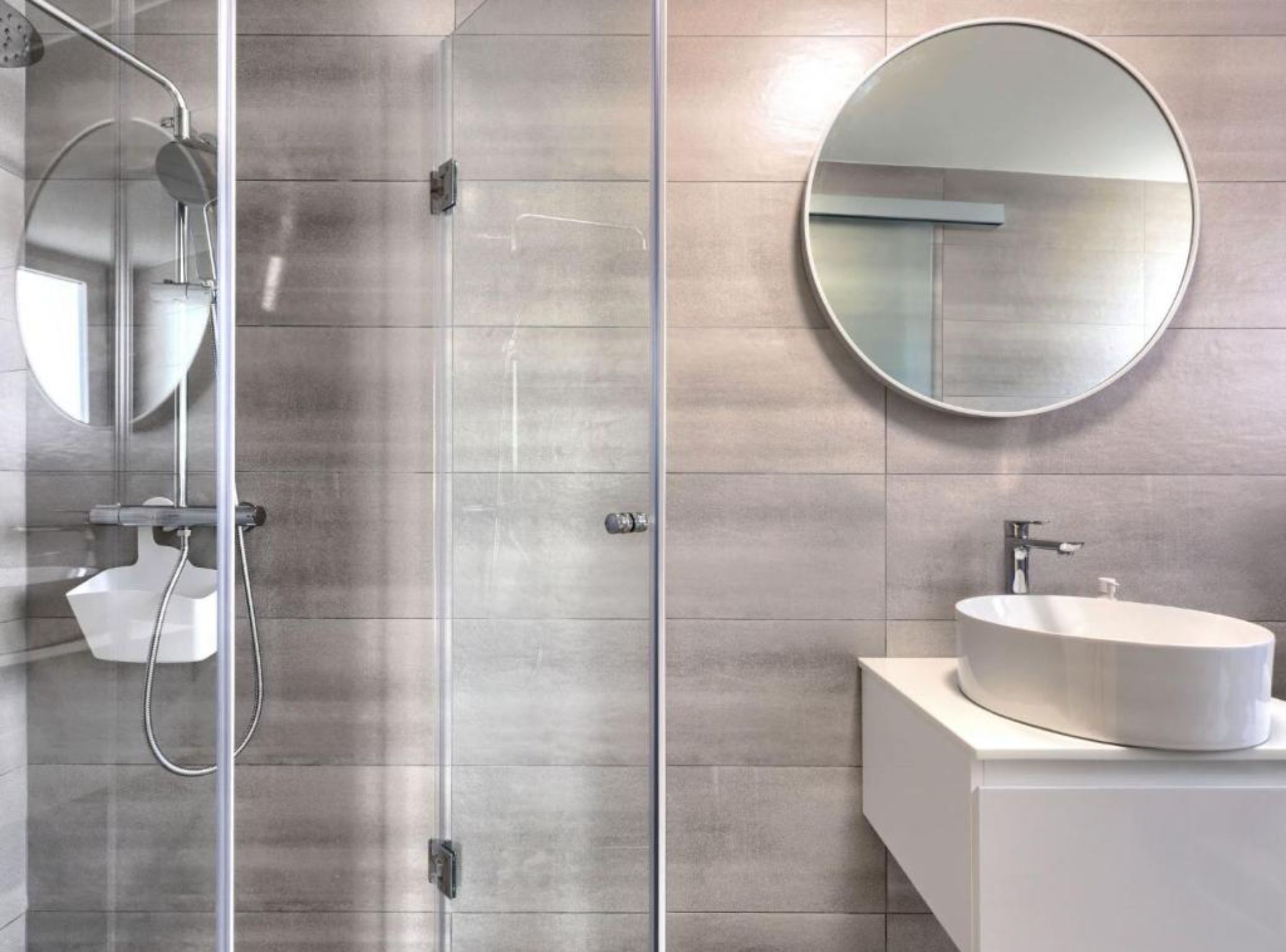 Une salle de bain moderne avec une douche à parois de verre, un miroir rond et un lavabo blanc.