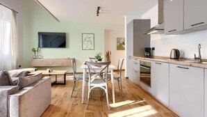 A modern kitchen with white cabinets, a wooden countertop, and a built-in oven. There is a dining area with a wooden table and chairs, and a sofa in the foreground. - Apartments Zanet & Niccolo (Fazana)
