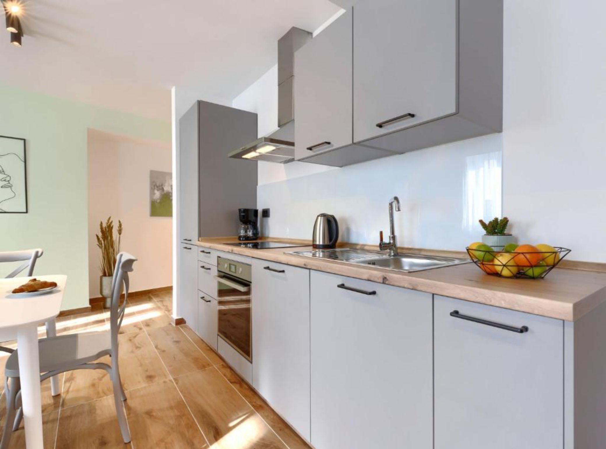 A modern kitchen with white cabinets, a stainless steel sink, and a countertop with a coffee maker and kettle.