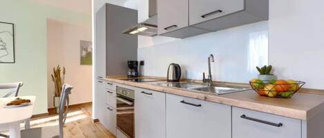 A modern kitchen with white cabinets, a stainless steel sink, and a countertop with a coffee maker and kettle.