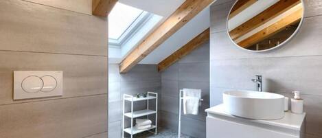 A modern bathroom with a skylight, a round mirror, and a white sink.