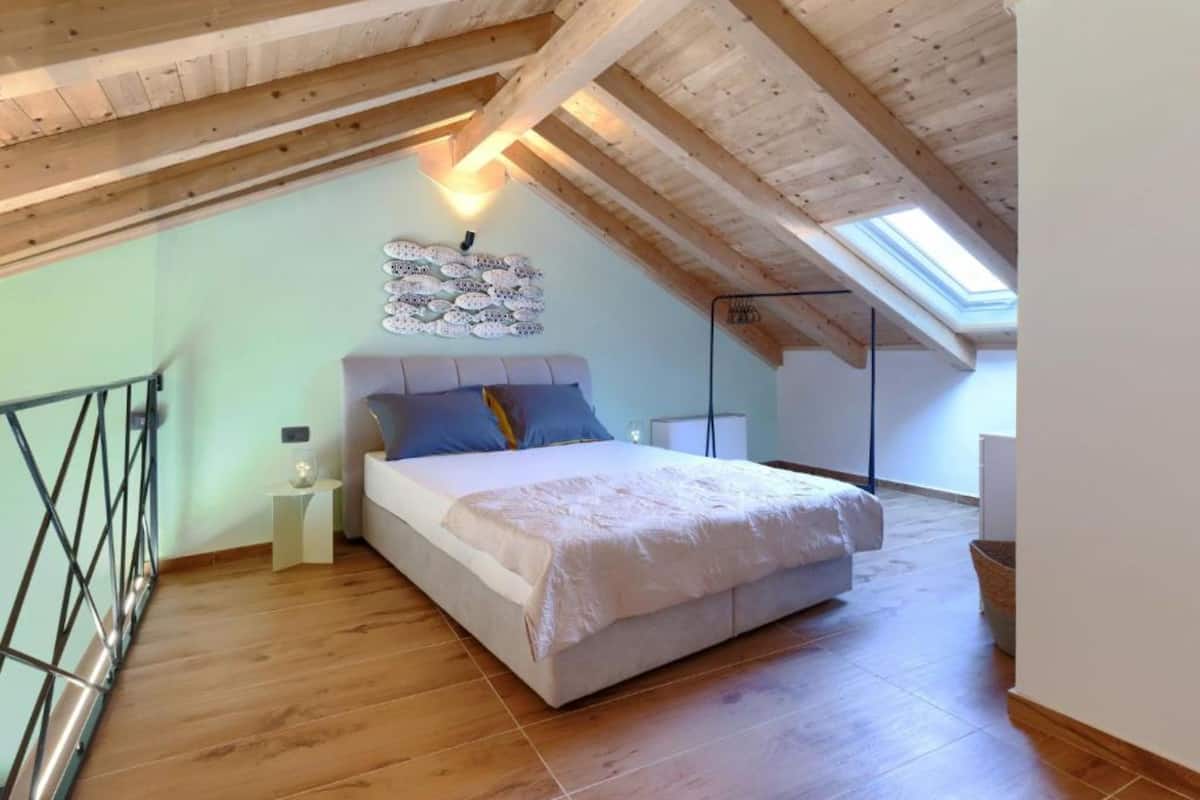 Un dormitorio con techo inclinado, una cama, una lámpara de pared y un tragaluz.