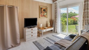 Uma sala de estar moderna com televisão, painel de parede de madeira, sofá e porta de vidro deslizante que dá para um jardim.