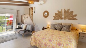 Quarto com cama, sofá, escrivaninha, espelho e vista para o exterior.