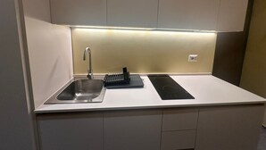 A compact kitchen with a stainless steel sink, a black induction cooktop, and a built-in oven. - Atelier 12 (Milan)