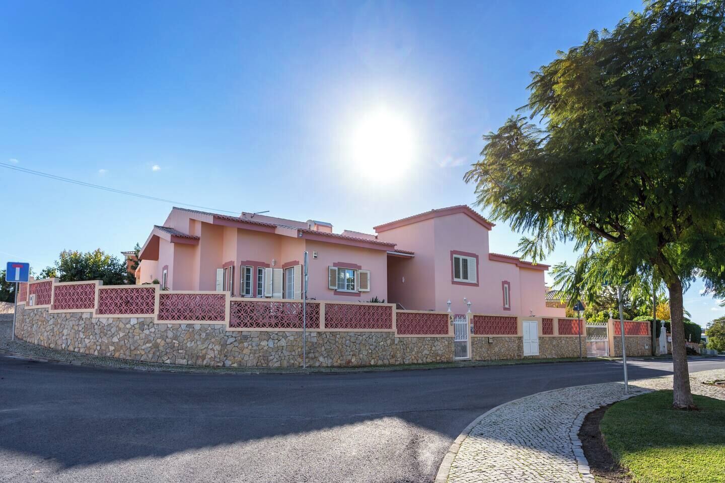 Una casa rosa con un muro de piedra y un camino de entrada pavimentado.