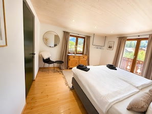 A bedroom with a bed, a chair, a small table, a dresser, and a window with a view.