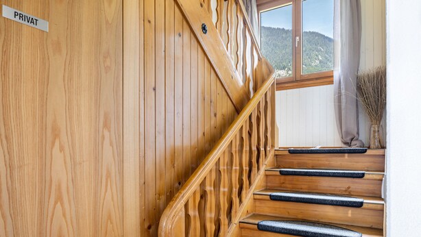 Una escalera de madera con un letrero que dice 'PRIVAT', que conduce a una habitación con ventana con vistas a un paisaje boscoso.