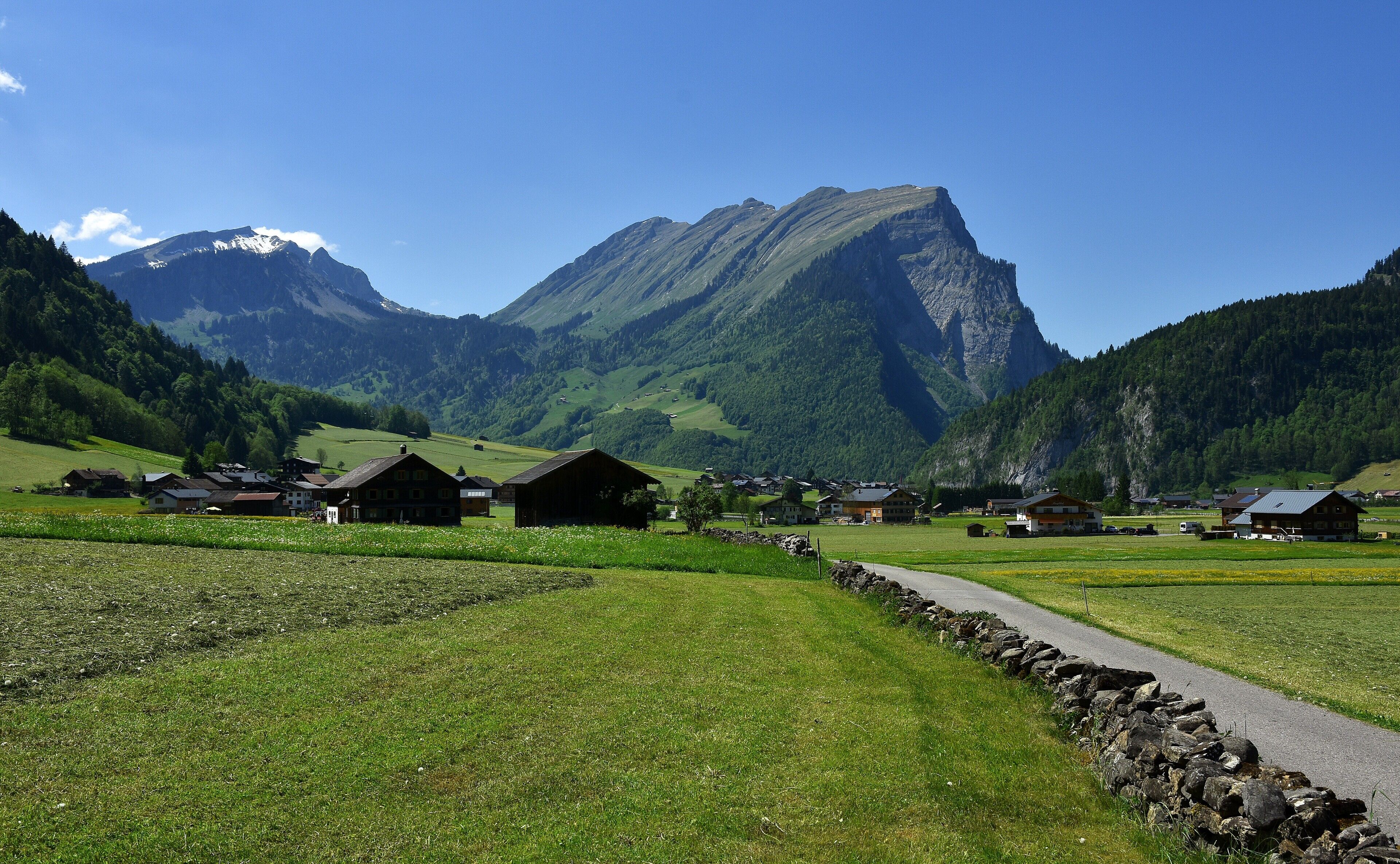 Ein ländliches Dorf mit traditionellen Häusern, einer Steinmauer und einem Berg im Hintergrund.