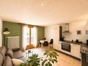 A modern kitchen with a dining area, a sofa, and a plant.