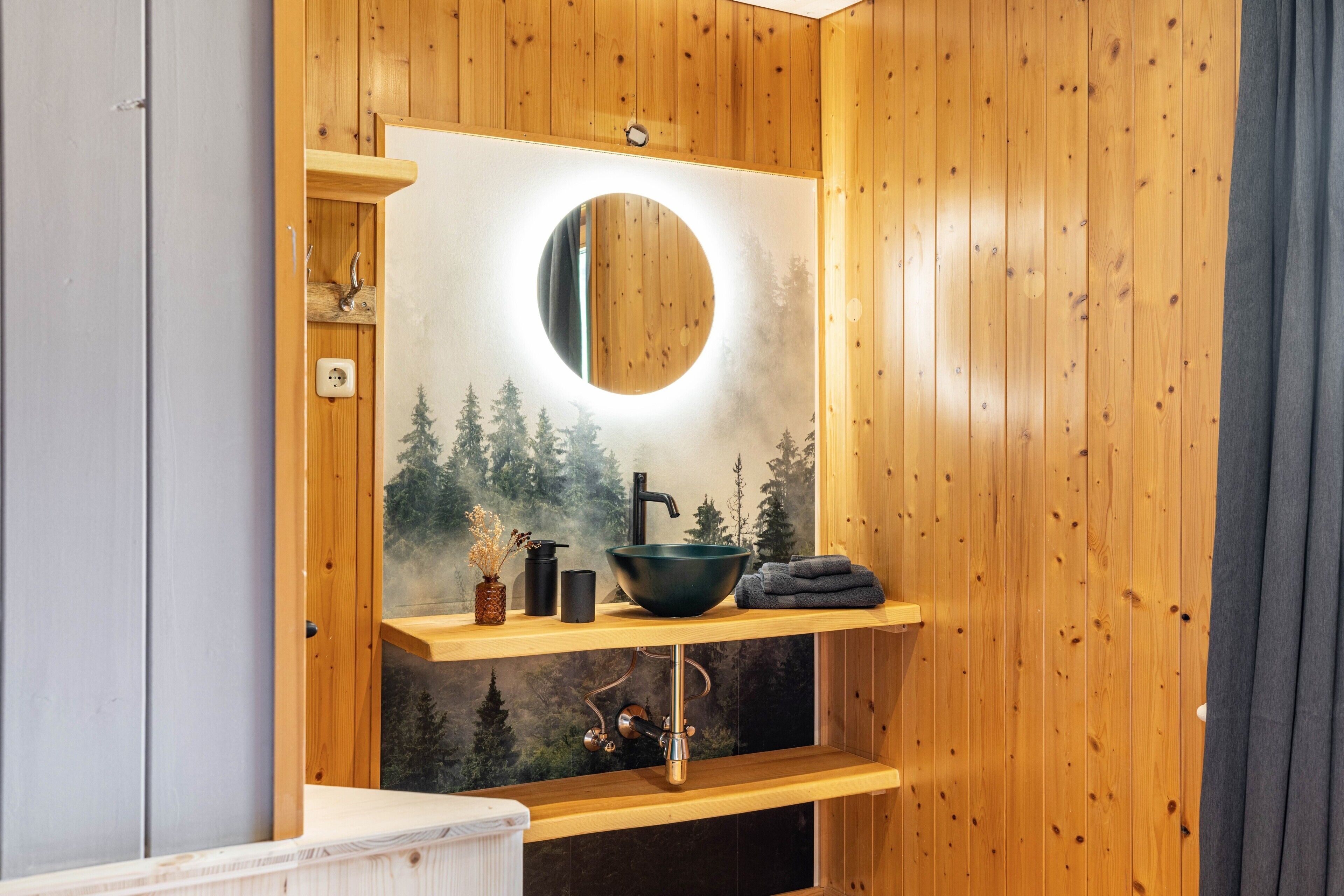 Interior de una cabaña de madera con espejo de marco de madera, lavamanos y un perchero para toallas.