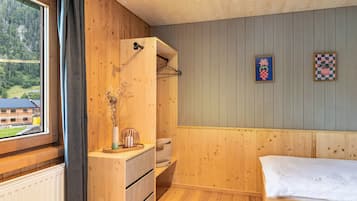 Una habitación con paredes de madera, una cama, un aparador, un ventanal con vista a un edificio y un estante de pared con un jarrón.
