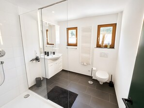 Et moderne badeværelse med et glasbadeværelse, en hvid vask, toilet og et vindue med udsigt.