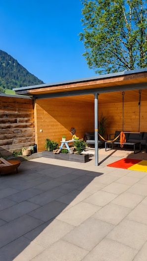 Un espace extérieur abrité, avec un mur en bois, une table et des chaises, et une vue sur une montagne.