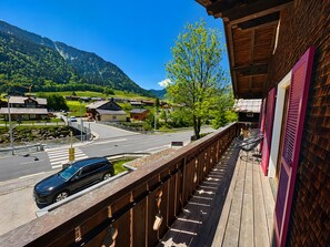 En balkon med udsigt over en vej, en bil og et bjerglandskab.