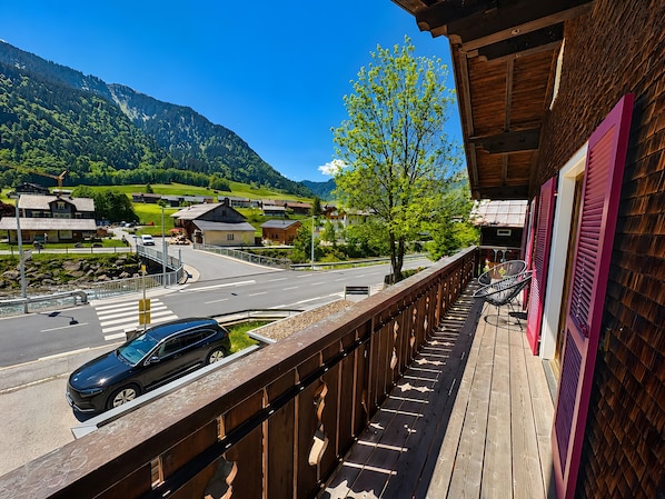 A balcony with a view of a road, a car, and a mountain landscape.