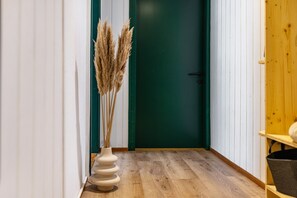 A hallway with a wooden floor, a green door, and a white vase with dried plants. - Apartment “Wälderblick” with Mountain View, Shared Terrace and Wi-Fi (Au)