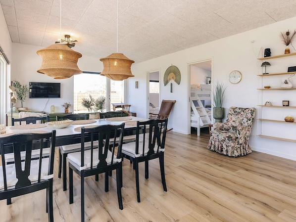 A dining area with a wooden table and chairs, a TV mounted on the wall, and a ceiling fan. - 4 Star Holiday Home in Skibby (Skibby)
