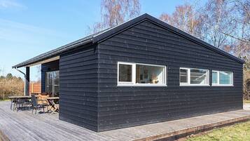 A black wooden cabin with a deck, large windows, and a visible outdoor seating area.