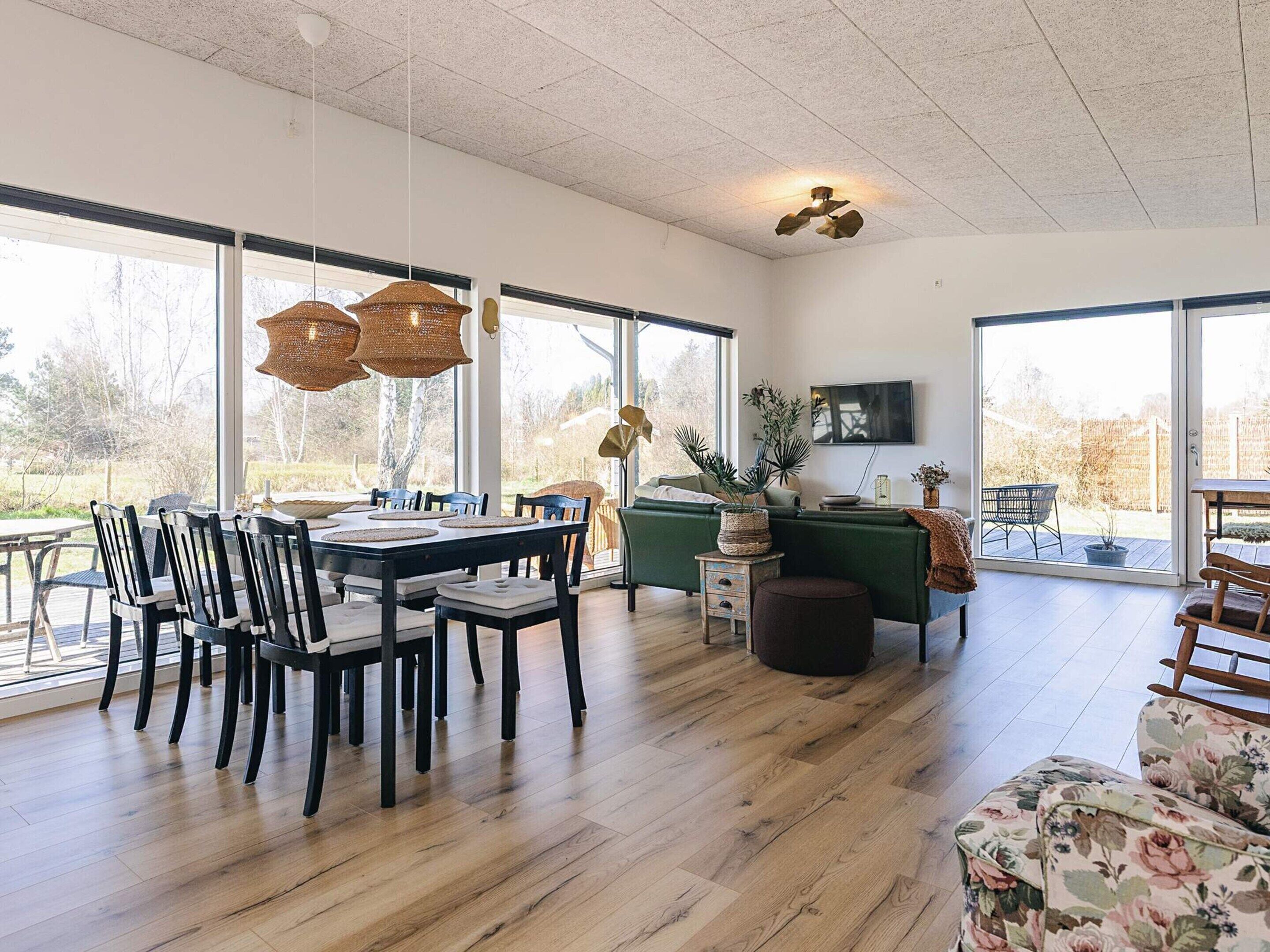 Tilava olohuone, jossa on ruokapöytä, tuoleja, sohva ja seinälle asennettu televisio.
