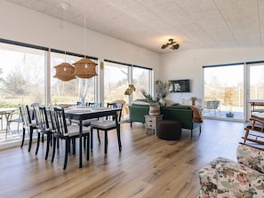 A spacious living area with a dining table, chairs, a sofa, and a TV mounted on the wall. - 4 Star Holiday Home in Skibby (Skibby)