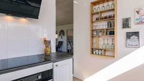 Una cocina con armarios blancos, encimera negra y repisa de madera con cristalería.