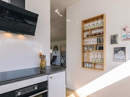 Una cocina con armarios blancos, encimera negra y repisa de madera con cristalería.