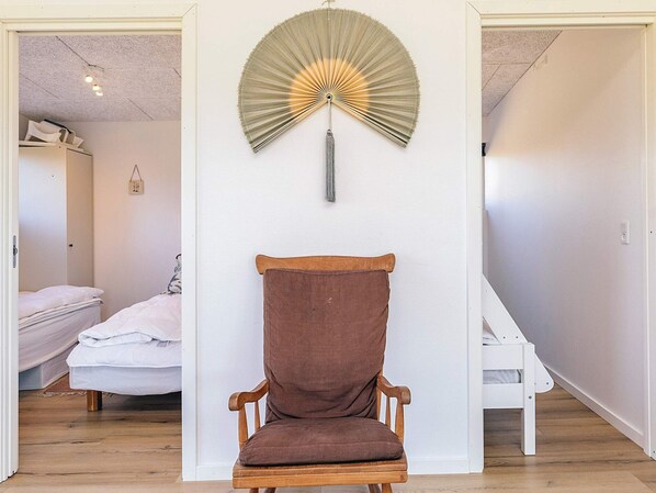 Ein Zimmer mit einem hölzernen Stuhl, einem Bett und einem Wandventilator.