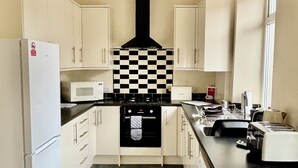A compact kitchen with white cabinets, a black and white checkered backsplash, a black range hood, a microwave, a toaster, and a sink.