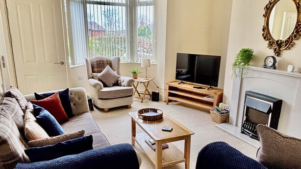 A living room with a sofa, armchairs, a coffee table, a TV, and a fireplace.