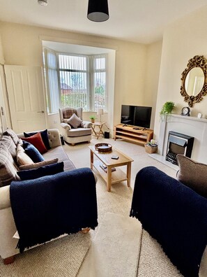 Un saló amb un sofà, butaques, una taula de centre, un televisor i una llar de foc.