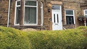 A stone-built house with a number '195' on the door, a bay window, and a small garden area.
